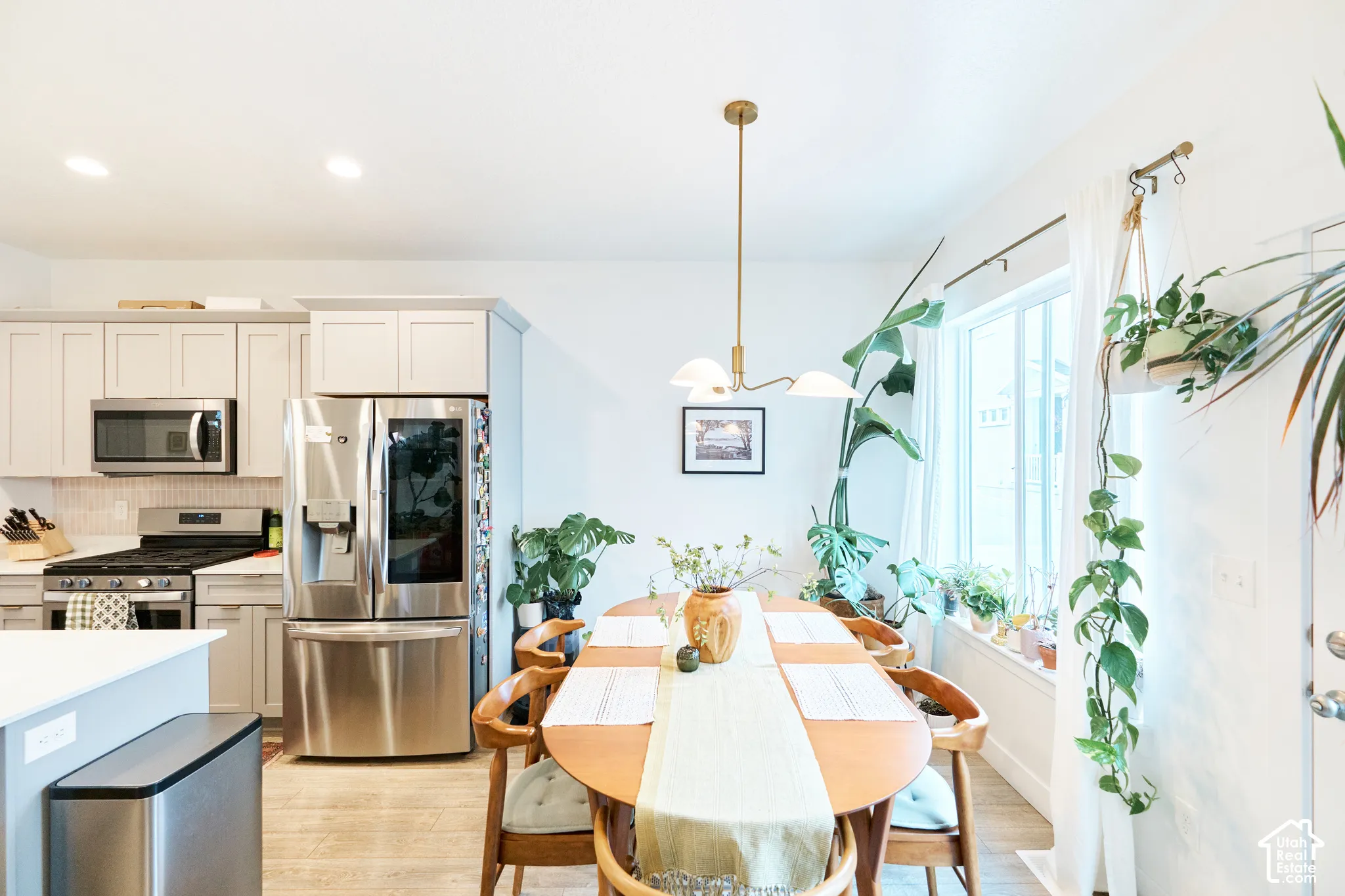 Kitchen featuring light-toned cabinetry, stainless steel appliances, a multi-light brass pendant fixture, and wood-finish flooring