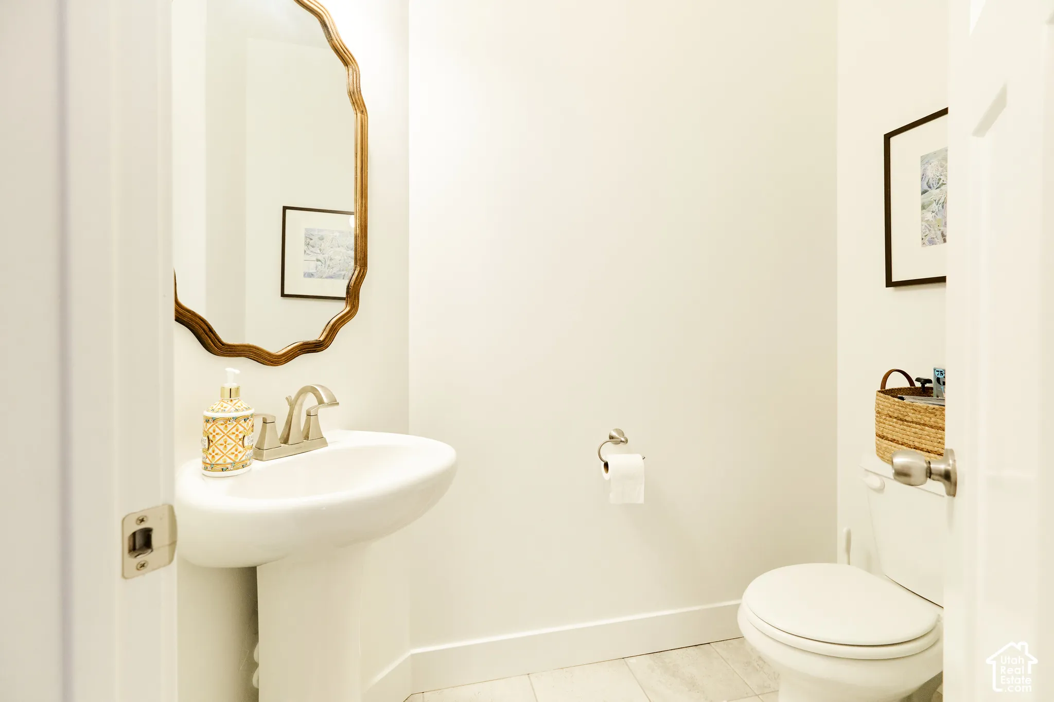 Powder room featuring a pedestal sink, brushed-nickel faucet, scalloped-edge wall mirror, and tile flooring