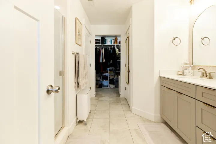 Bathroom featuring a light-toned vanity with cabinet storage, arched mirror, tiled flooring, and a glass-enclosed shower