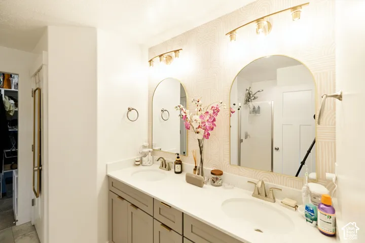 Dual-sink vanity featuring grey cabinetry, solid-surface countertops, twin arched mirrors, and two three-light vanity fixtures