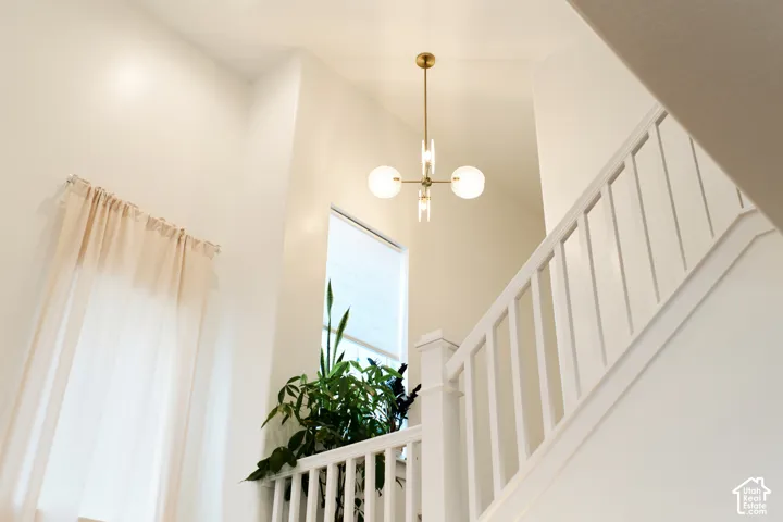 Vaulted ceiling featuring a brass multi-globe pendant chandelier, white-painted wood railing, and vertical window