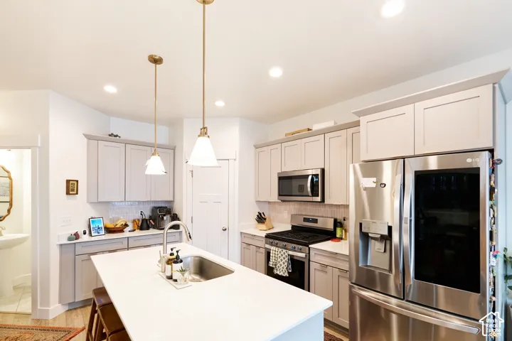 Kitchen featuring shaker-style cabinetry, a central island with an undermount sink, quartz countertops, stainless steel appliances, and pendant lighting