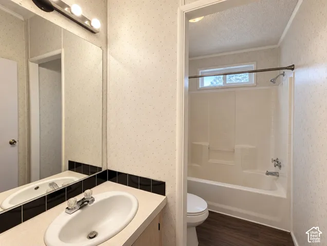 Bathroom featuring a vanity with a drop-in sink, wall-mounted mirror with multi-bulb light fixture, tub-shower combination, transom window, and wood-finish flooring