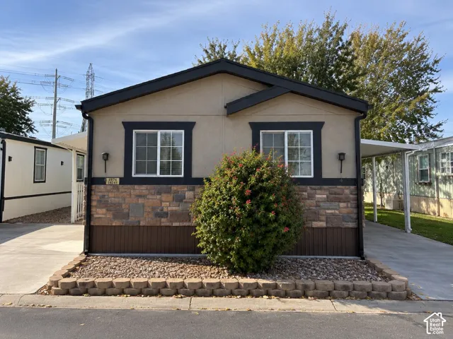 Single-level exterior featuring tan stucco siding, a stone veneer wainscot, concrete driveway, and a stacked-block garden border