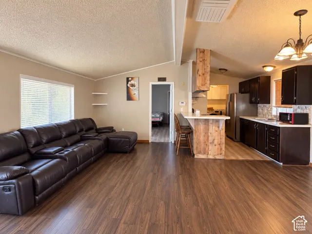 Open-concept living space featuring wood-finish flooring, vaulted ceilings, a breakfast bar with natural wood detailing, and dark-toned cabinetry