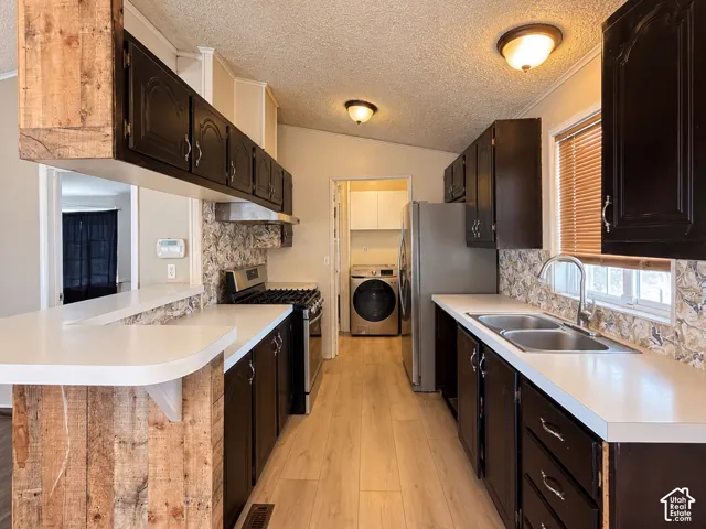 Kitchen featuring dark cabinetry, wood-finish flooring, a breakfast bar with reclaimed wood detailing, stainless steel appliances, and a dual-basin sink