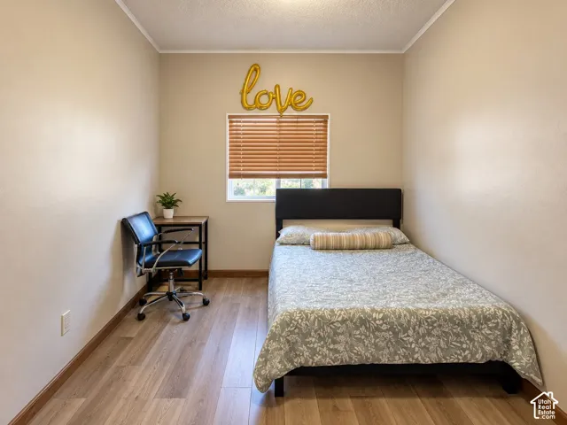 Bedroom featuring neutral wall paint, wood-finish flooring, and a single window with horizontal blinds