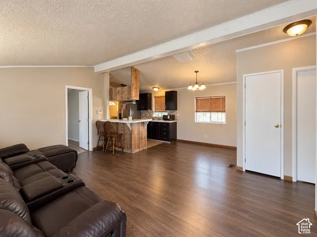 Open interior featuring wood-finish flooring, a kitchen breakfast bar with wood-panel siding, dark cabinetry, and multiple flush-mount and chandelier lighting fixtures