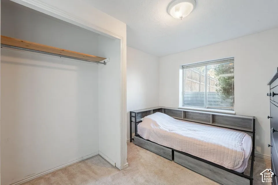 Carpeted flooring featuring a walk-in closet with an upper wooden shelf and hanging bar, a built-in wooden headboard with open shelving, a sliding glass window, and a flush-mount ceiling light fixture