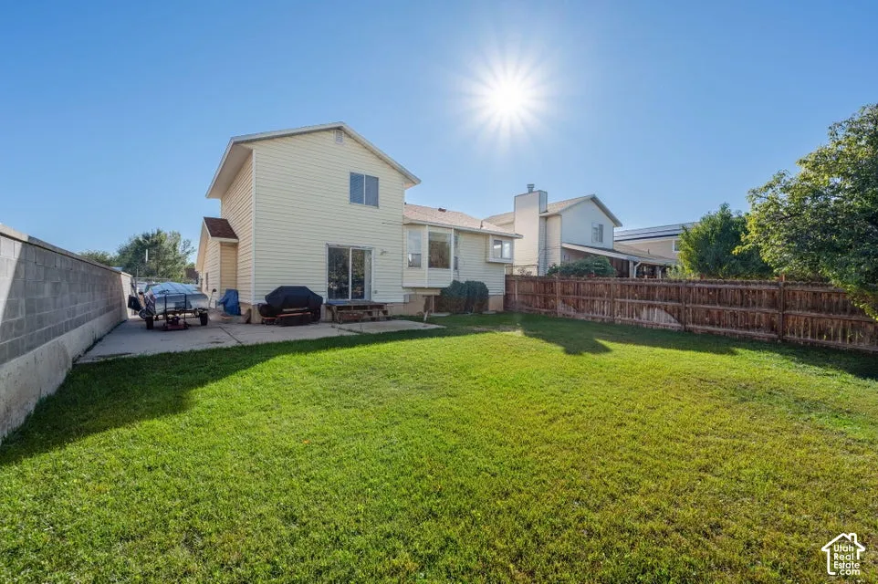 Backyard featuring a grass lawn, concrete patio, wood fence, and masonry wall