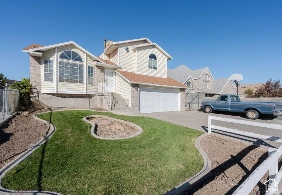 Split-level exterior featuring vinyl siding, stone veneer accents, an attached two-car garage, and a landscaped front yard with concrete edging