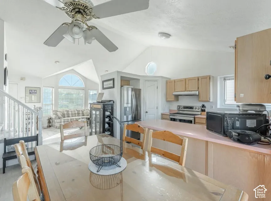 Kitchen featuring wood cabinetry, a breakfast bar, stainless steel appliances, and a vaulted ceiling with an overhead light and fan fixture