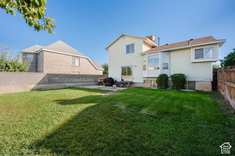 Backyard featuring a manicured lawn, concrete patio, perimeter masonry wall, and wood-fence enclosure
