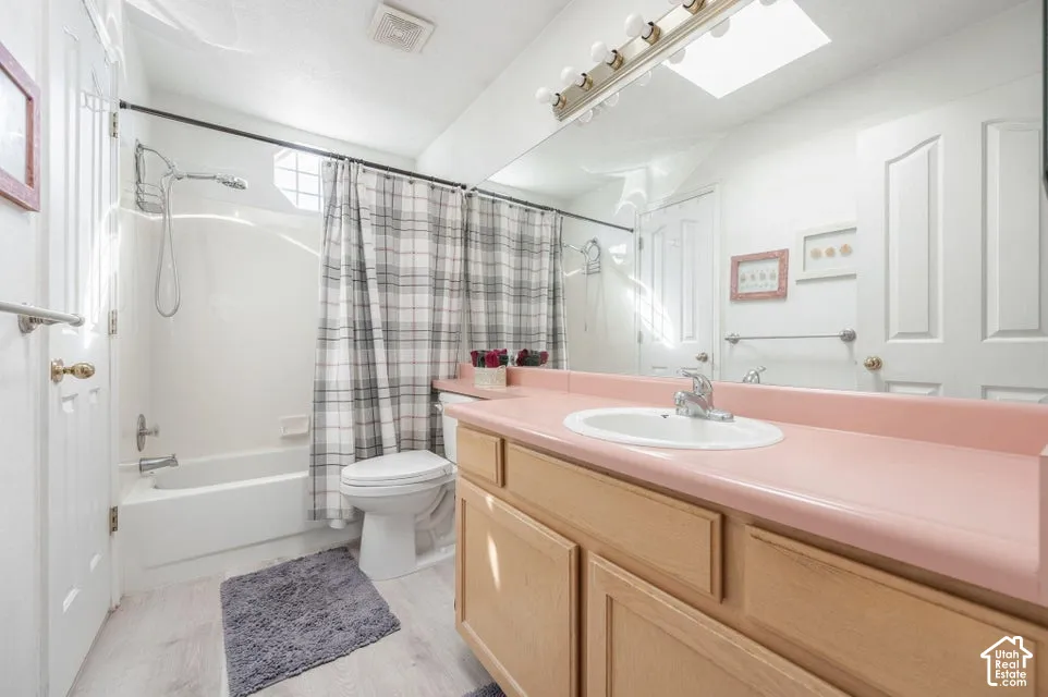 Bathroom featuring a vanity with wood-finish cabinetry, a solid-surface countertop, an oval undermount sink, a full-width wall mirror, and a tub-shower combination with a surround