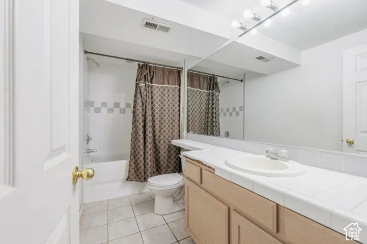 Bathroom featuring a vanity with tile countertop, integrated oval sink, full-width wall mirror, and a tile-surround shower and tub combination