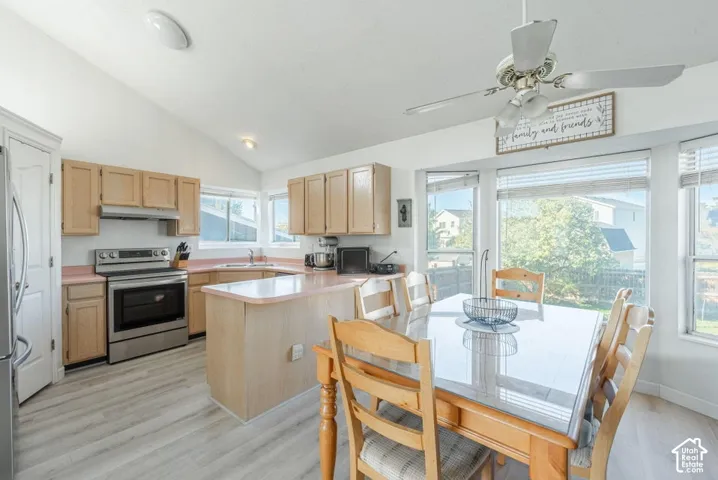 Kitchen featuring wood-finish cabinetry, light-toned laminate countertops, stainless steel electric range with hood, vaulted ceilings, and wood-finish flooring