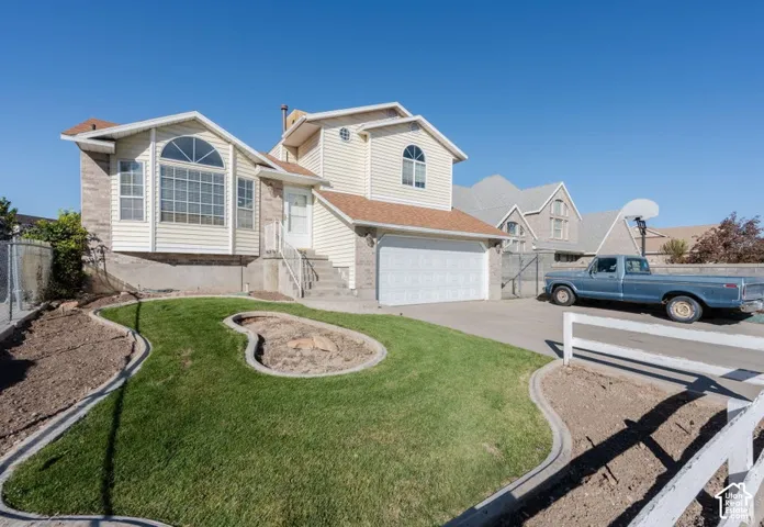 Split-level exterior featuring vinyl siding, stone veneer accents, an attached two-car garage, and a landscaped front yard with concrete edging