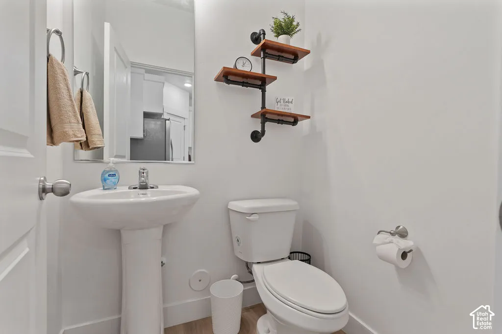 Powder room featuring a pedestal sink, chrome faucet, wall-mounted mirror, and wood-finish flooring