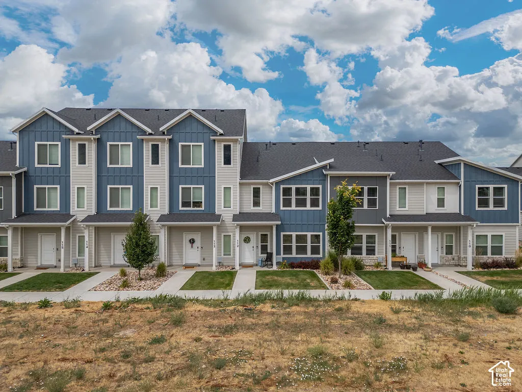 Multi-story townhome exterior featuring vertical board-and-batten siding, horizontal lap siding, stone veneer accents, pitched roofs, and concrete walkways