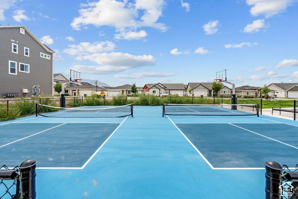 Dual recreational courts featuring a multi-use surface, integrated pickleball nets, and basketball hoops, enclosed by perimeter chain-link fencing