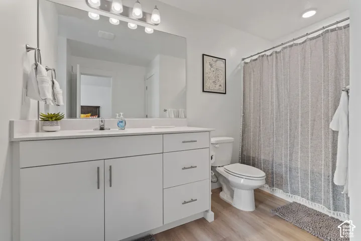 Bathroom featuring a white vanity with drawers and cabinet storage, stone-surface countertop, full-width mirror, multi-bulb light fixture, and wood-finish flooring