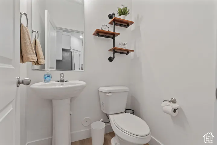 Powder room featuring a pedestal sink, chrome faucet, wall-mounted mirror, and wood-finish flooring