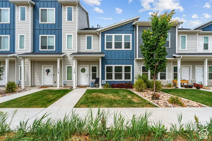 Multi-level townhouse exterior featuring a combination of horizontal lap siding and vertical board-and-batten siding, concrete walkways, and landscaped lawn areas with stone ground cover