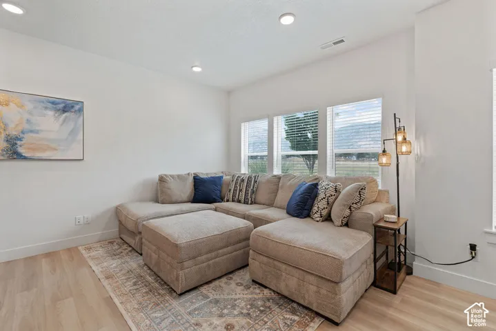 Bright interior space featuring wood-finish flooring, recessed lighting, and a trio of windows with horizontal blinds