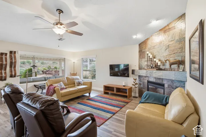 Living room featuring a floor-to-ceiling stone fireplace, wood-finish flooring, vaulted ceilings, and a ceiling fan