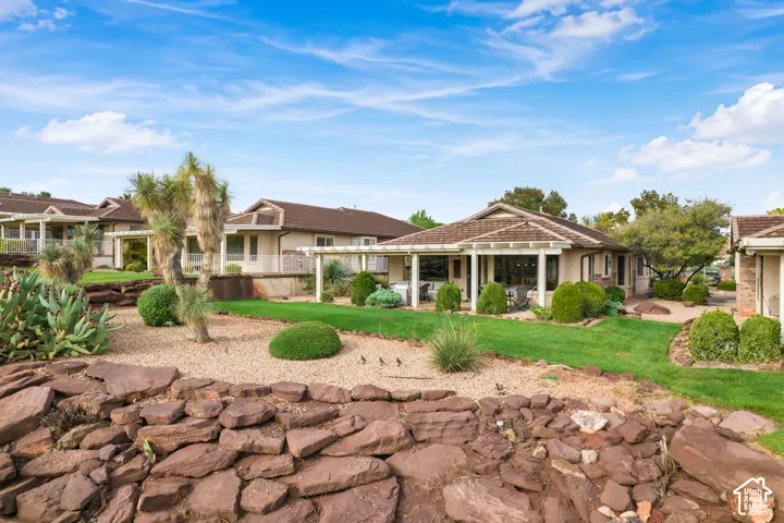 Backyard featuring a tiered stone retaining wall, manicured lawn, xeriscaping, and a covered patio with white structural columns