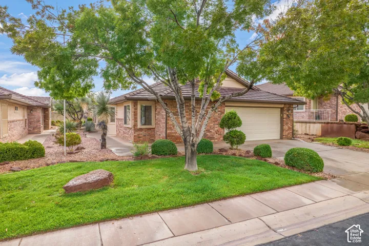 Single-story brick exterior featuring a multi-car garage, tile roofing, concrete driveway, and manicured landscaping with mature trees