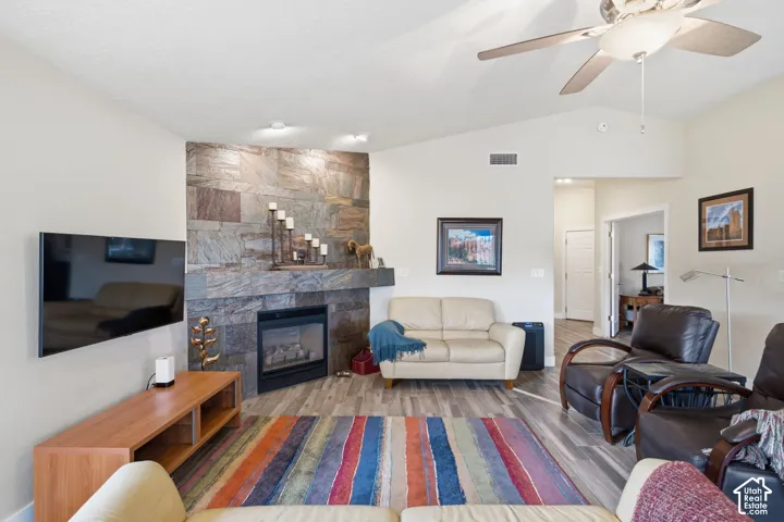 Corner fireplace featuring a floor-to-ceiling stone-tile surround, mantel, wood-finish flooring, and vaulted ceilings with an integrated paddle fan