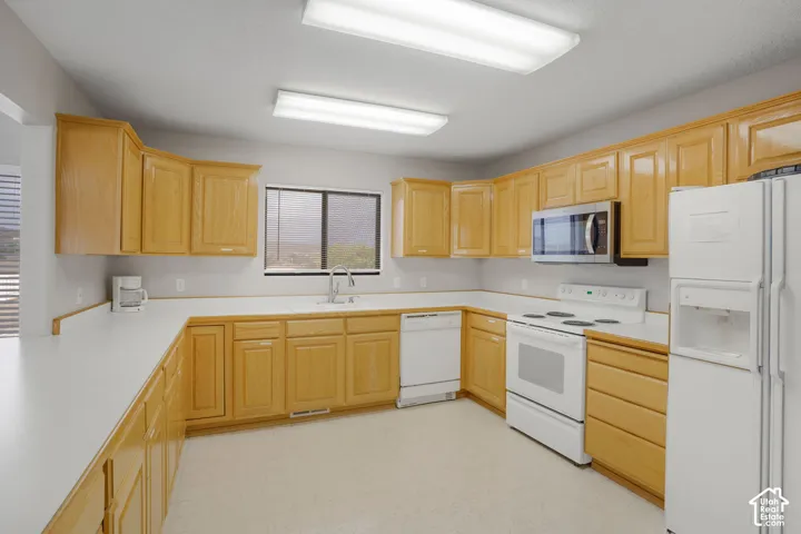Kitchen featuring natural wood-finish cabinetry, white solid-surface countertops, dual fluorescent lighting fixtures, and white appliances including a built-in microwave