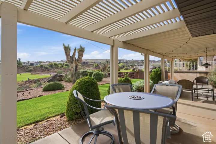 Covered concrete patio featuring a louvered pergola, landscaped lawn, mature shrubbery, and stone rock-work