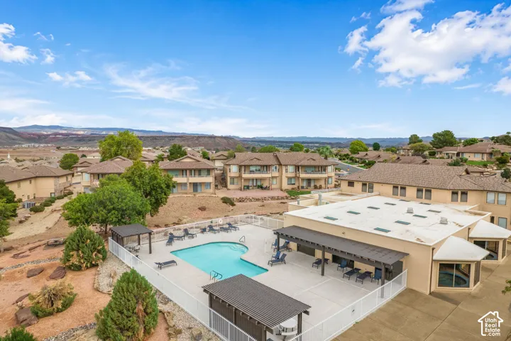Community swimming pool featuring a concrete deck, pergola-covered lounge space, white perimeter fencing, and desert landscape surroundings