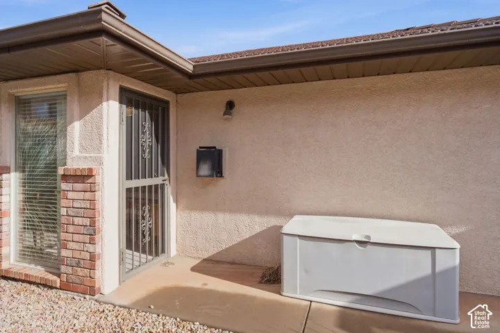 Stucco exterior featuring a metal screen door, brick masonry accents, concrete porch, and fixed-pane window