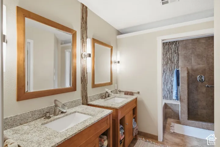 Dual-sink vanity with stone countertops, wood-finish cabinetry, framed mirrors, and a walk-in shower with decorative vertical tile accents