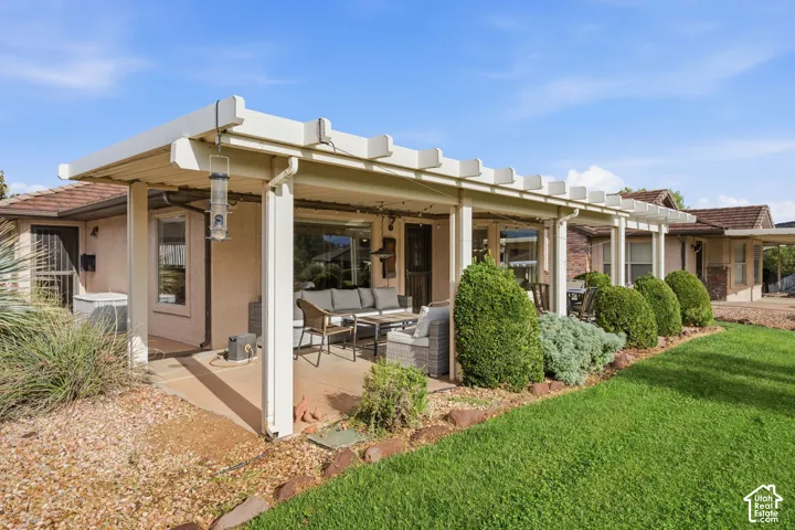 Extended covered patio featuring a white pergola structure, concrete flooring, manicured lawn, and low-maintenance landscaping with decorative stone borders