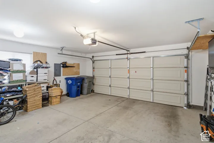 Two-car garage featuring a concrete floor, automated overhead sectional door, ceiling-mounted light fixtures, and overhead storage shelving