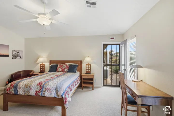 Neutral-toned bedroom featuring carpeted flooring, a white ceiling fan with integrated lighting, and a security-screened door providing exterior access