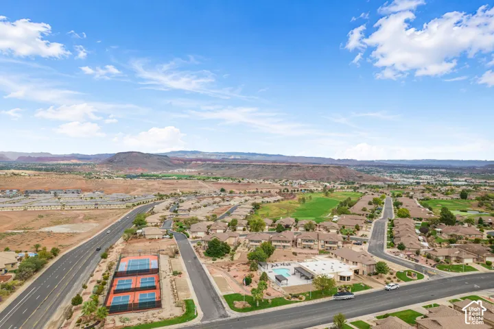 Aerial perspective of a community featuring tennis courts, a swimming pool, arid desert landscaping, and prominent mountain backdrops
