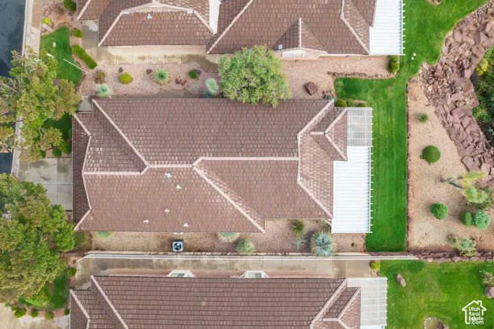 Aerial perspective of a residence featuring a brown tile roof, an attached white pergola, a dedicated concrete driveway, and established landscaping including a grass lawn and mature trees