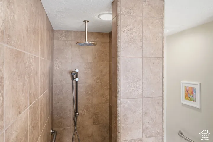 Shower enclosure featuring floor-to-ceiling tile, ceiling-mounted rainfall showerhead, adjustable handheld shower wand, and wall-mounted grab bars