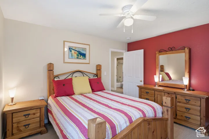 Neutral-toned room featuring a red accent wall, ceiling fan with integrated lighting, carpeted flooring, and a multi-panel interior door