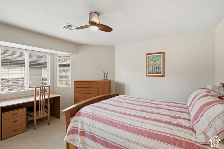Neutral-toned room featuring a bay window, wall-to-wall carpeting, and a ceiling-mounted light fixture with a fan