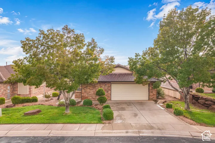 Single-story brick exterior featuring a tiled roof, multi-car garage, concrete driveway, and mature landscaping