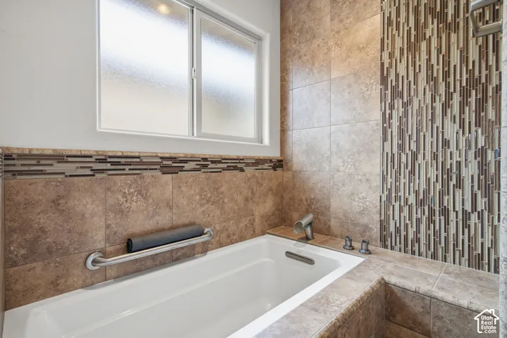 Soaking tub featuring large-format tile surround, decorative linear mosaic tile inlay, integrated brushed metal hardware, and a frosted glass window