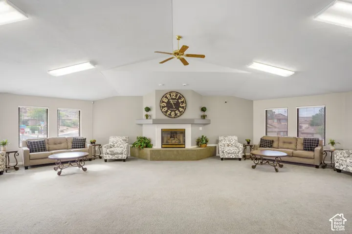 Expansive interior featuring a vaulted ceiling with multiple rectangular light fixtures, a central ceiling fan, and a fireplace with a stone-finish hearth