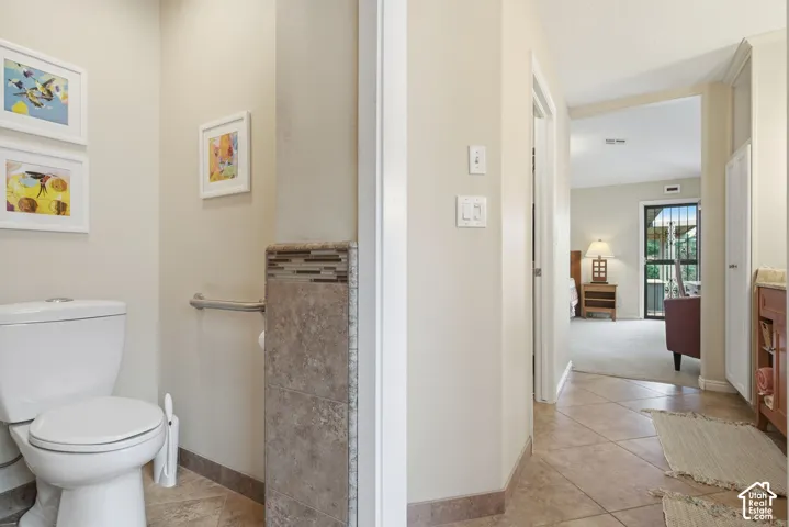 Ceramic tile flooring, stone-tiled wall accent, wall-mounted safety grab bar, and neutral wall tones