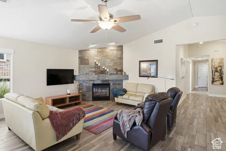 Vaulted ceiling with a central brushed nickel ceiling fan, floor-to-ceiling natural stone fireplace surround, and wood-finish tile flooring